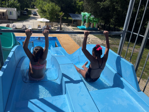 Two children sit at the top of a blue water slide at Campsite Les Franquettes holiday park in Nouvelle-Aquitaine, France.
