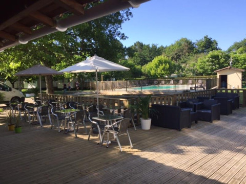 Outdoor terrace with tables, chairs, and umbrellas next to a fenced swimming pool in a green setting.