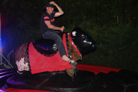 A man wearing a hat rides a mechanical bull at night at Campsite Les Franquettes in Nouvelle-Aquitaine, France.