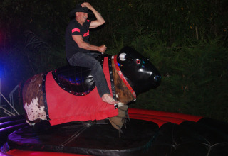 A man wearing a hat rides a mechanical bull at night at Campsite Les Franquettes in Nouvelle-Aquitaine, France.