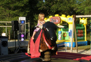 Una bambina gioca su un toro meccanico davanti a un castello gonfiabile al campeggio Les Franquettes.