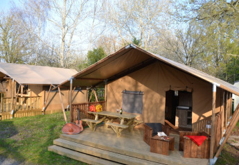 Tente safari Lodge Woody 27 avec terrasse en bois, banquettes rustiques, guitare et cadre boisé.