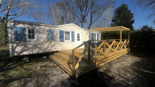 Premium Mobile Home Spa mit Holzterrasse, blauen Fensterläden und Bäumen unter blauem Himmel.