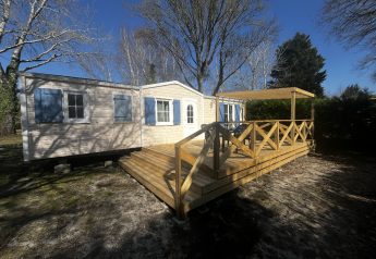 Premium Mobile Home Spa mit Holzterrasse, blauen Fensterläden und Bäumen unter blauem Himmel.