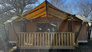 Foto van de Luxury Lodge XXL safaritent met grote houten veranda en geel canvas dak in de zon.