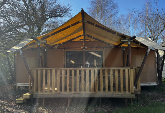 Foto af en stor luksus safari-telt, Luxury Lodge XXL, med træveranda og gul teltdug i solen.