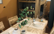 Zona pranzo rustica nella tenda safari Lodge Woody 27 con mobili in legno, tavolo apparecchiato e letto a castello.