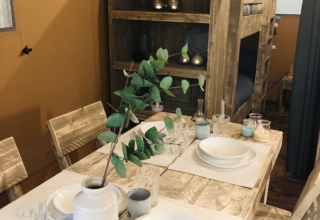 Rustikaler Essbereich im Safari-Zelt Lodge Woody 27 mit Holzmöbeln, gedecktem Tisch und Etagenbett.