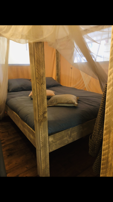 Bett mit Holzrahmen und Moskitonetz in einem Safari-Zelt Lodge Woody 27 auf dem Campingplatz Les Franquettes.