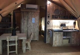 Binnenzicht van het Lodge 'Woody 27' safaritent met houten meubels op Camping Les Franquettes in Frankrijk.
