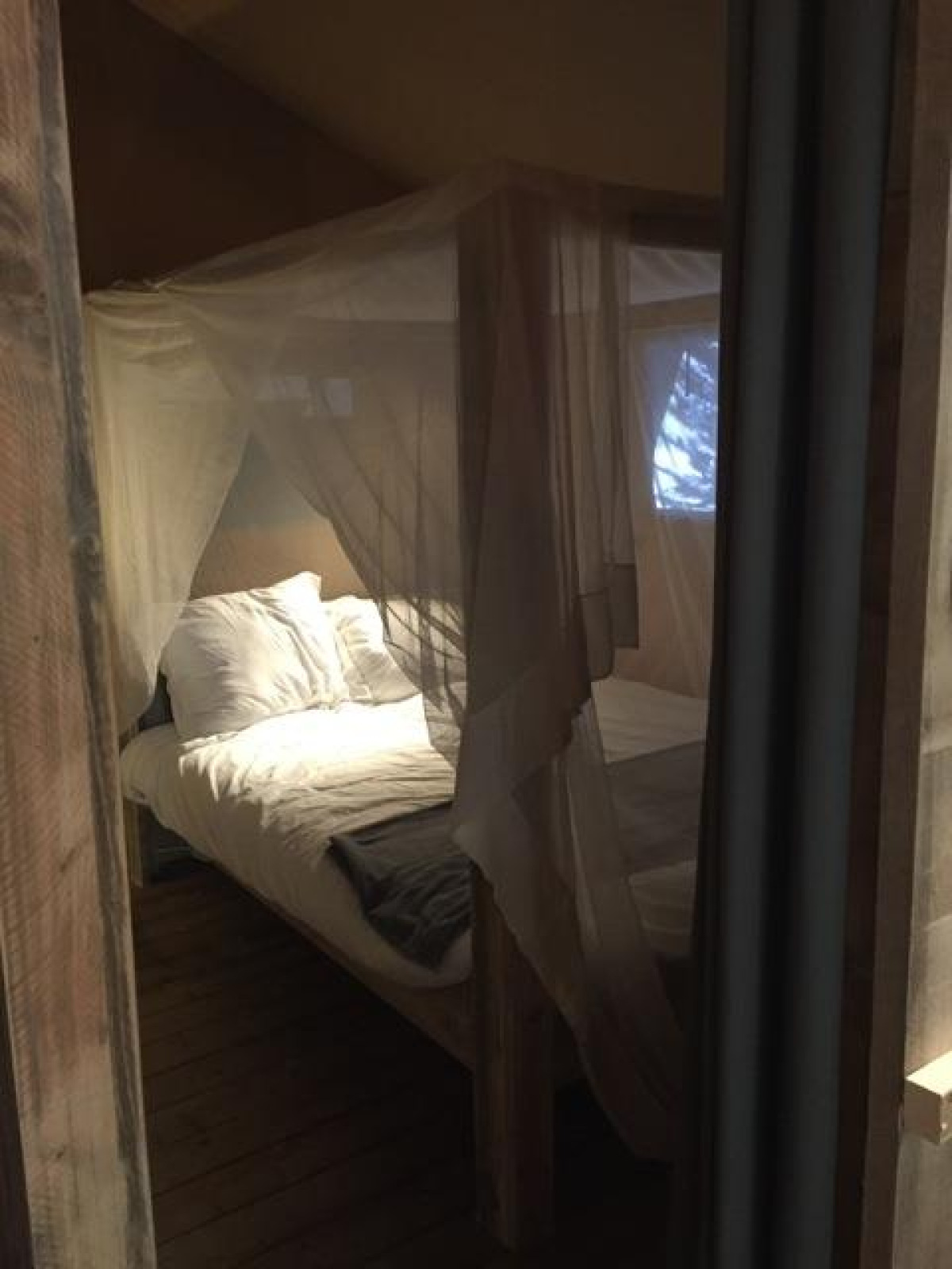 Interieur van safaritent Lodge Woody 27 met muskietennet en bed op Camping Les Franquettes, Frankrijk.