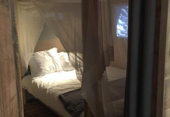 Interno della tenda safari Lodge Woody 27 con zanzariera e letto al campeggio Les Franquettes, Francia.