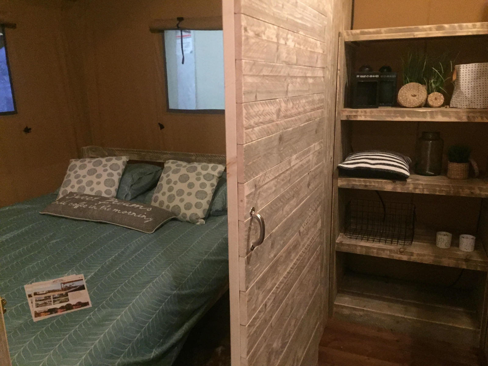 Binnenkant safaritent Lodge Woody 38 op Camping Les Franquettes, Frankrijk, met bed en boekenplank.