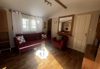 Wohnzimmer im Premium Mobile Home auf dem Campingplatz Les Franquettes mit roten Sofas und Tageslicht.