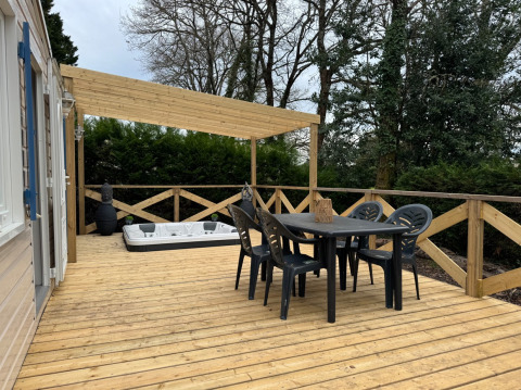 Træterrasse med spisebord, stole, spabad og overdækning ved Premium Mobile Home på Camping Les Franquettes.