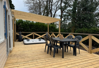 Wooden deck with dining table, chairs, hot tub, and pergola at Premium Mobile Home at Campsite Les Franquettes.