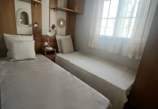 Værelse med to enkeltsenge, lyse gardiner og træmøbler i Premium Mobile Home på Les Franquettes campingplads.