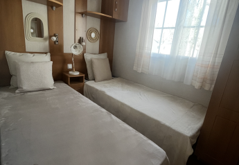 Camera con due letti singoli e mobili in legno nel Premium Mobile Home al campeggio Les Franquettes in Francia.