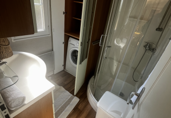 Badezimmer im Premium Mobile Home am Campingplatz Les Franquettes mit Duschkabine, Waschmaschine und Fenster.