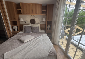 Premium Mobilheim Schlafzimmer mit Doppelbett, Holzschränken und Blick auf Terrasse mit Whirlpool, Frankreich.