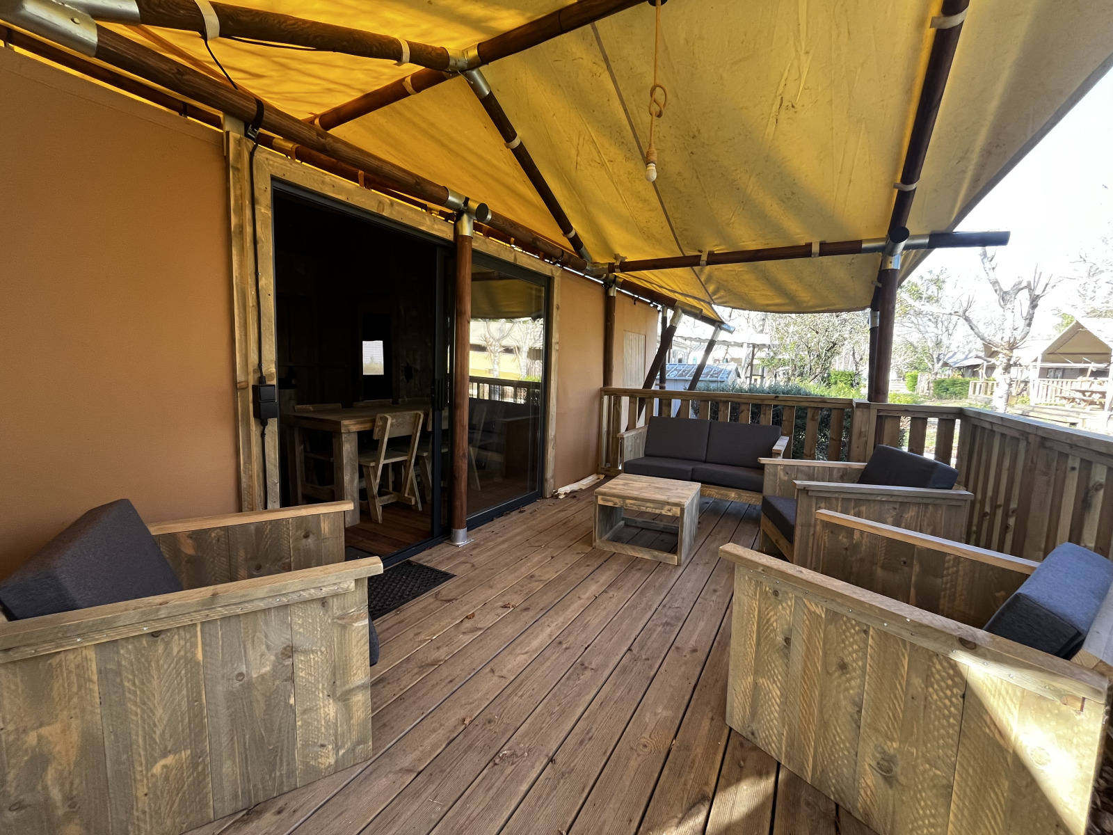Overdekt houten terras met comfortabele zitplaatsen in Luxury Lodge XXL op Camping Les Franquettes, Frankrijk.