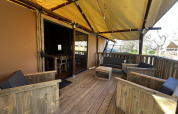 Terraza de madera cubierta con asientos en tienda Luxury Lodge XXL en el camping Les Franquettes, Francia.