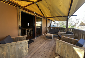 Terraza de madera cubierta con asientos en tienda Luxury Lodge XXL en el camping Les Franquettes, Francia.