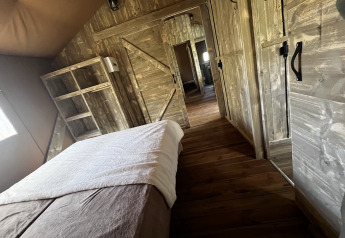 Vista interna di una tenda safari di lusso con arredi in legno al campeggio Les Franquettes in Francia.