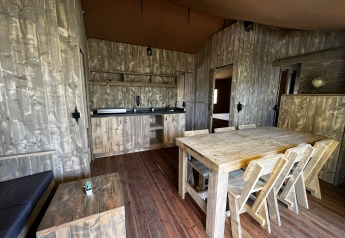 Interior de la tienda safari Luxury Lodge XXL en el camping Les Franquettes en Francia, con muebles de madera.