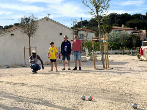 Four people play pétanque on a gravel court at Campsite Les Tamaris in Provence-Alpes-Côte d’Azur, France.