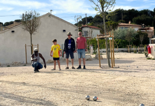 Quattro persone giocano a pétanque su un campo di ghiaia al campeggio Les Tamaris in Provenza-Alpi-Costa Azzurra, Francia.
