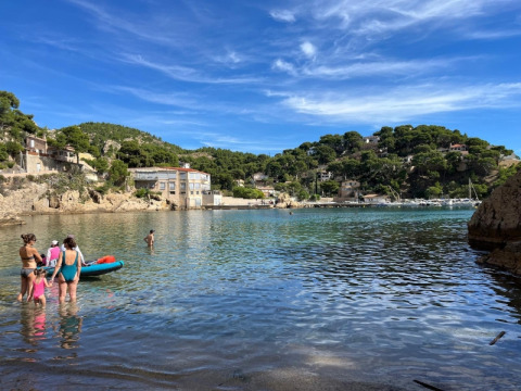 Persone che si godono il mare e il sole vicino a La Couronne, Martigues, tra colline verdi e case pittoresche.