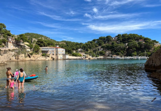 Persone che si godono il mare e il sole vicino a La Couronne, Martigues, tra colline verdi e case pittoresche.