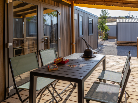 Terraza exterior en casa móvil Premium con mesa, sillas, sombrero y juegos, rodeada de otros chalets.