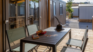 Outdoor terrace at Premium mobile home with table, chairs, hat, and games, surrounded by other chalets.