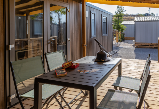 Outdoor terrace at Premium mobile home with table, chairs, hat, and games, surrounded by other chalets.