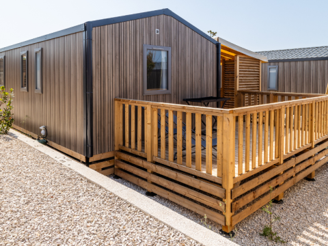 Premium Mobile Home Chalet auf hügeligem Gelände, mit Holzterrasse und moderner Außenansicht bei Sonnenlicht.
