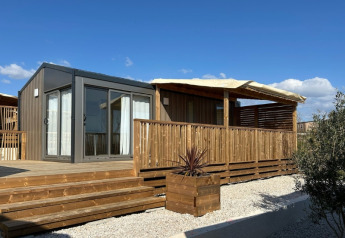 Chalet Premium Mobile Home Large con terraza de madera y ubicación en colina bajo el cielo azul.