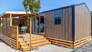 Premium Mobile Home chalet with wooden exterior and deck on a hillside location under blue sky.