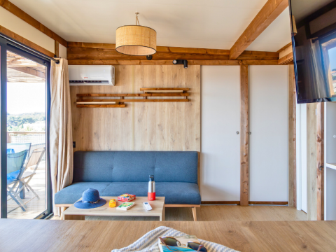Lichte, moderne leefruimte in het Premium chalet bij Camping Les Tamaris, met grijze zetel, tafel en terras.