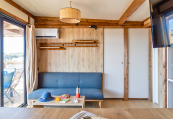 Soggiorno luminoso e moderno nel Premium chalet al Campeggio Les Tamaris, con divano grigio, tavolo e terrazza.