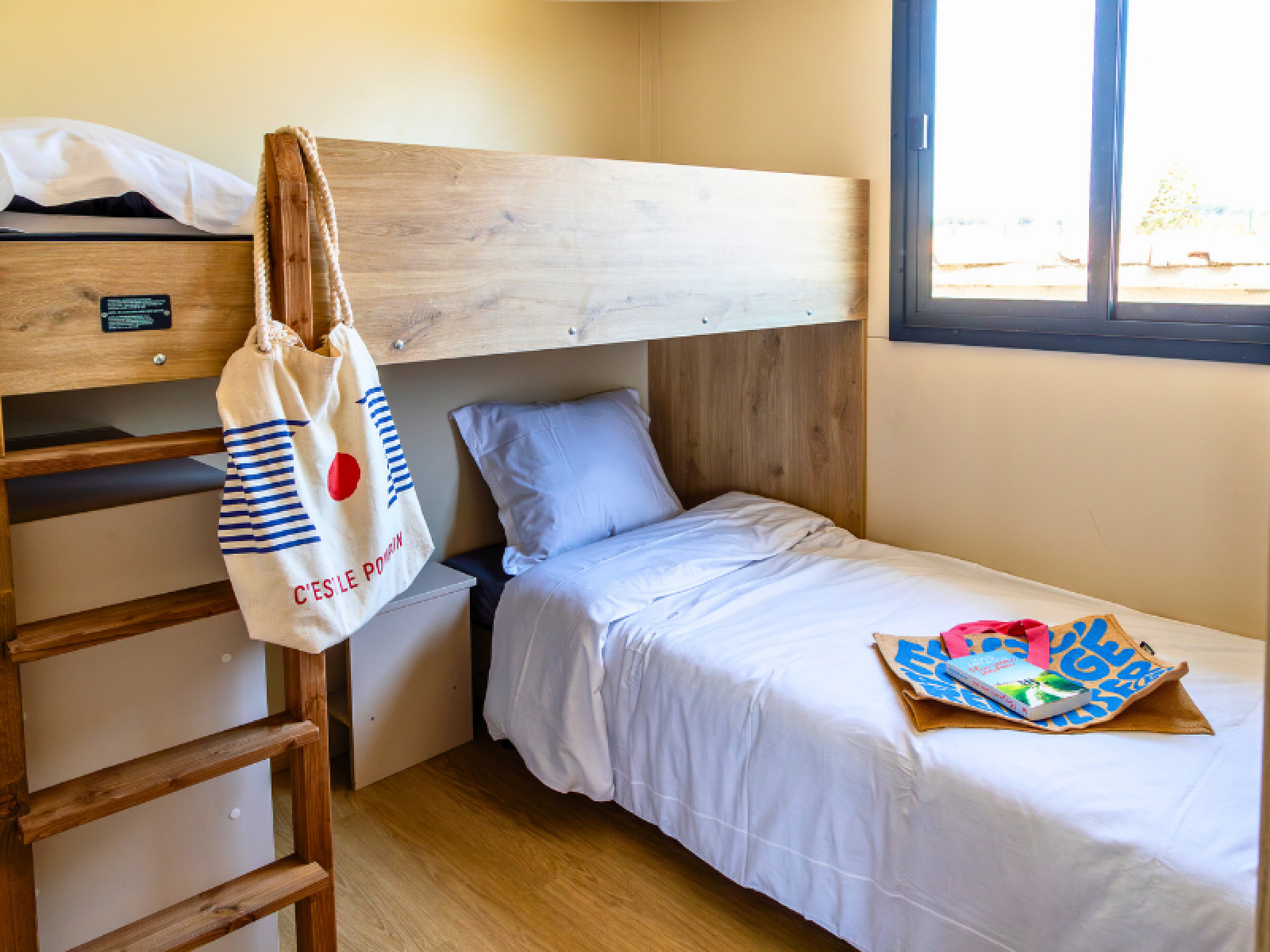 Kamer in het Premium chalet op Camping Les Tamaris in Frankrijk met stapelbed, tassen en raam.