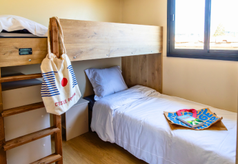 Habitación del chalet Premium en el Camping Les Tamaris en Francia con litera, bolsas y ventana.
