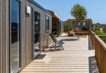 Wooden deck and outdoor seating at TRIBU mobile homes, Campsite Les Tamaris, France, on a sunny day.