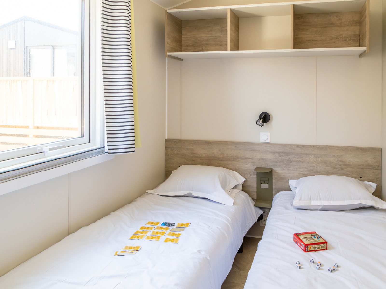 Moderne chaletkamer met twee eenpersoonsbedden, spelletjes, raam en planken bij Camping Les Tamaris, Frankrijk.