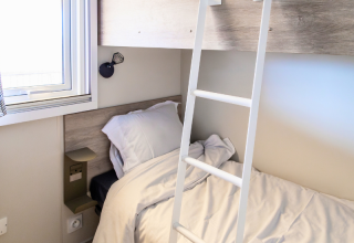 Camera chalet moderna con letto singolo, scala a soppalco, finestra luminosa e lampada da parete.
