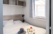 Bright bedroom in TRIBU mobile homes at Campsite Les Tamaris, France, with bed and large window.