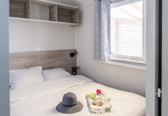 Bright bedroom in TRIBU mobile homes at Campsite Les Tamaris, France, with bed and large window.
