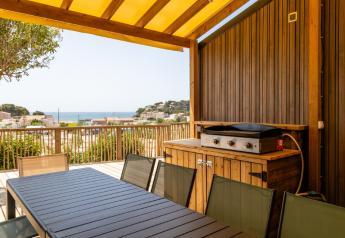 Covered outdoor dining area with grill and sea view at TRIBU mobile homes, Campsite Les Tamaris, France.