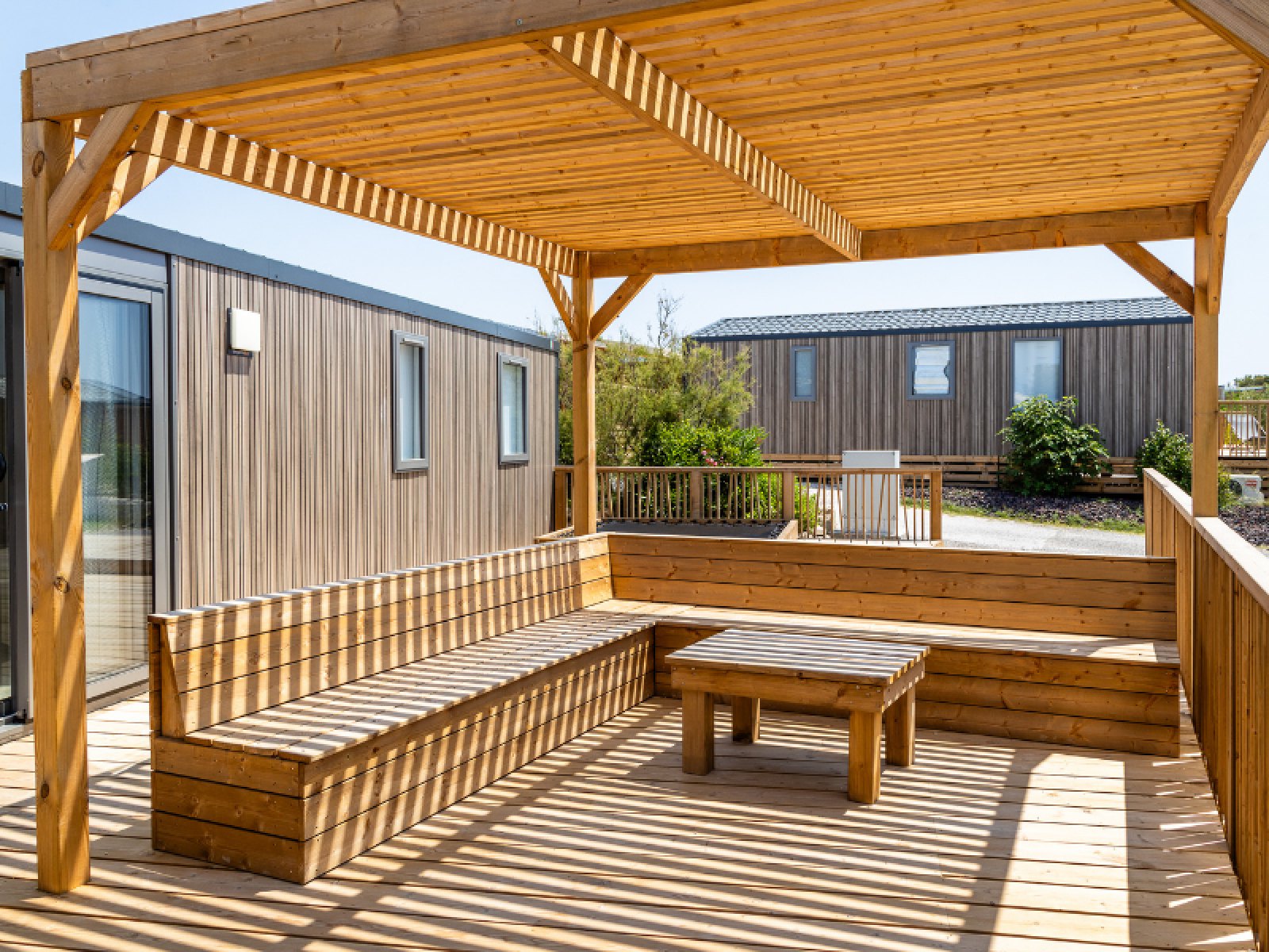 Houten terras met zitbanken en tafel bij TRIBU mobile homes op camping Les Tamaris in Frankrijk, onder pergola.